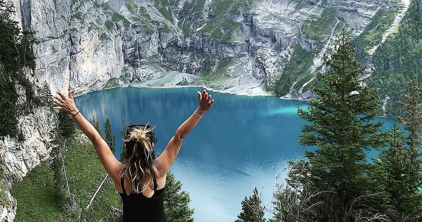 Bea de espaldas, con los brazos abiertos ante un lago de montaña